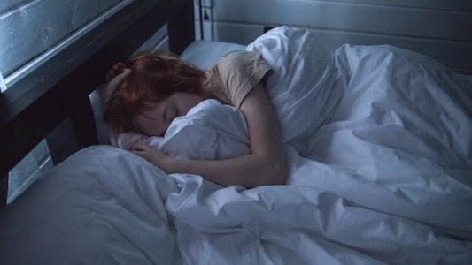Peaceful sleep benefits of mouth taping: woman resting under soft sheets in dimly lit bedroom.