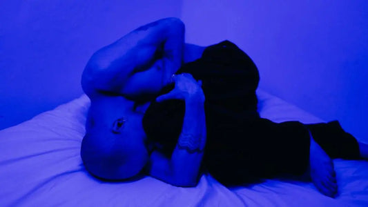 Bald man struggles with can't breathe through nose at night, depicted lying shirtless under blue light.